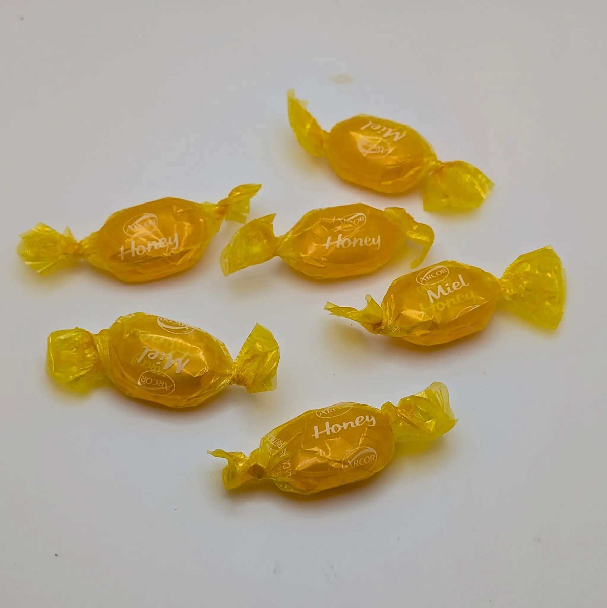 HONEY FILLED HARD CANDIES in translucent golden-yellow wrappers, individually twisted at both ends with honey lettering.