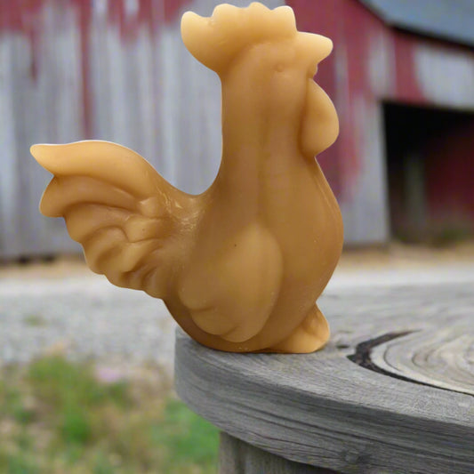 A beeswax candle shaped like a rooster chicken, placed on a floral patterned background.