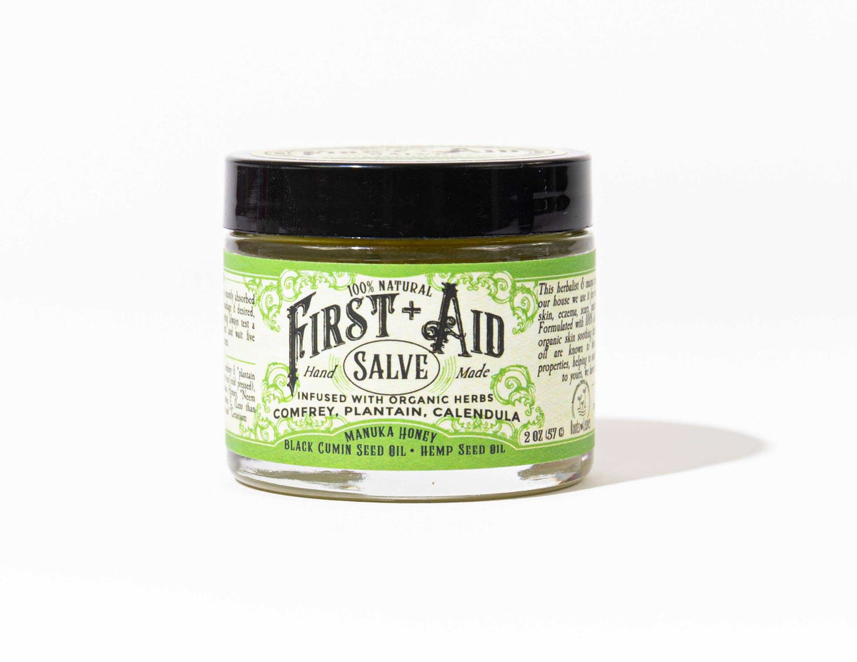 First Aid Salve in a clear round jar with a black lid and green-and-white botanical label, shown as a balm.