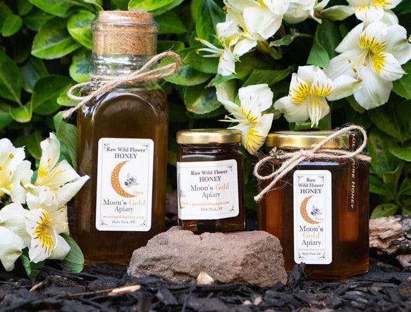 Wildflower Honey in three amber glass jars with gold lids, cork tops and rustic twine ties, bearing cream labels
