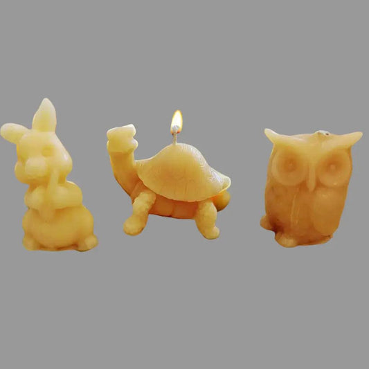 BEESWAX CANDLES : CRITTERS featuring three golden beeswax candles shaped like a bunny, turtle, and owl, with a lit wick.