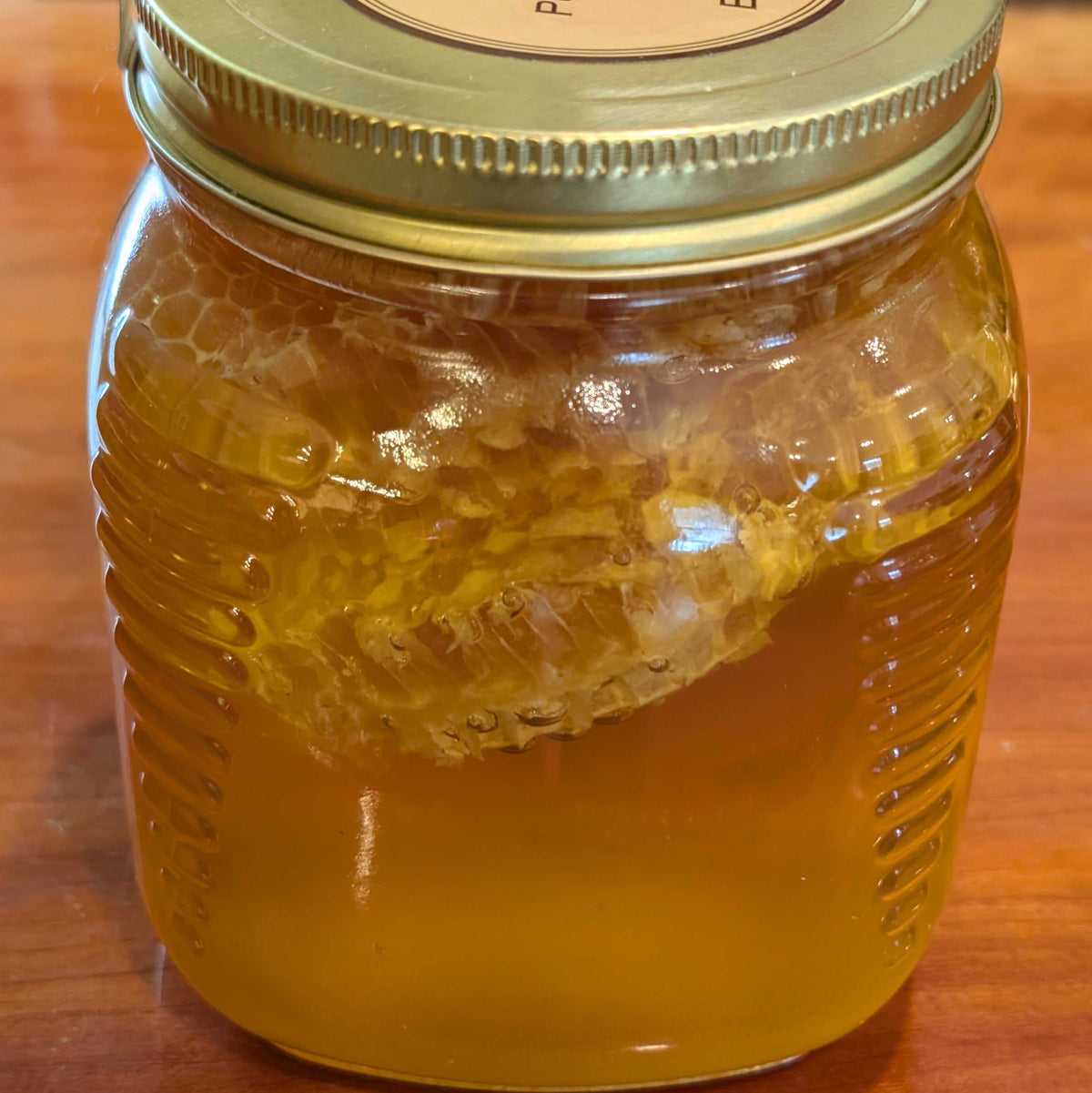 CHUNK COMB HONEY in a clear glass jar, golden amber honey with a large piece of pale honeycomb and a metal lid.