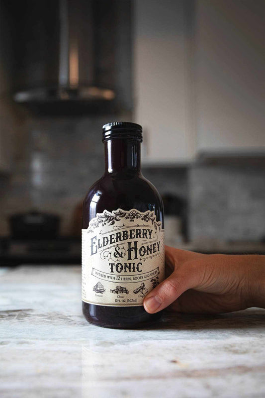 Elderberry and Honey Tonic in a dark amber glass bottle with a cream, ornate botanical label and black cap.