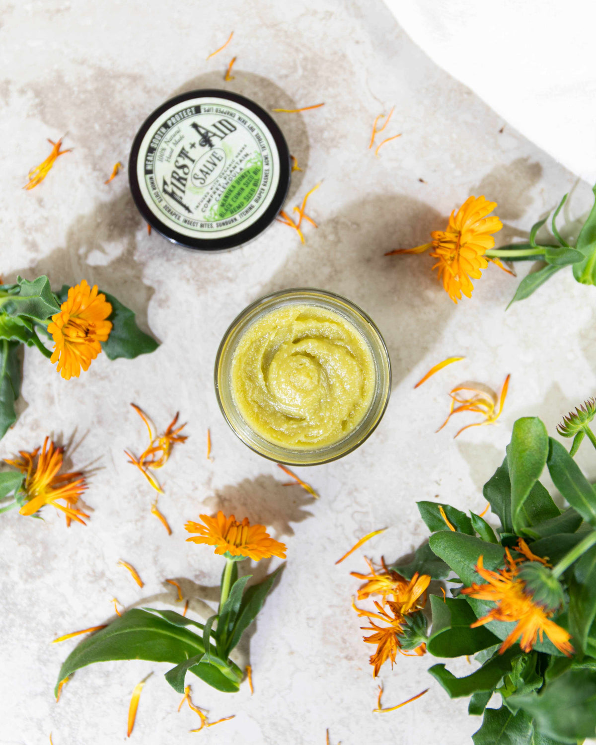 First Aid Salve in a black-lidded glass jar with a green-and-white label, shown as a textured yellow balm.