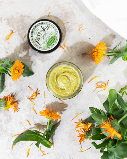 First Aid Salve in a black-lidded glass jar with a green-and-white label, shown as a textured yellow balm.