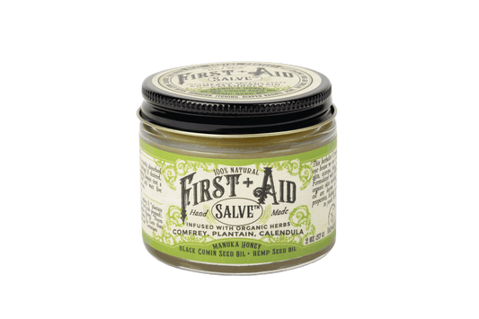 First Aid Salve in a clear glass jar with a black lid, pale yellow-green label and botanical detailing.