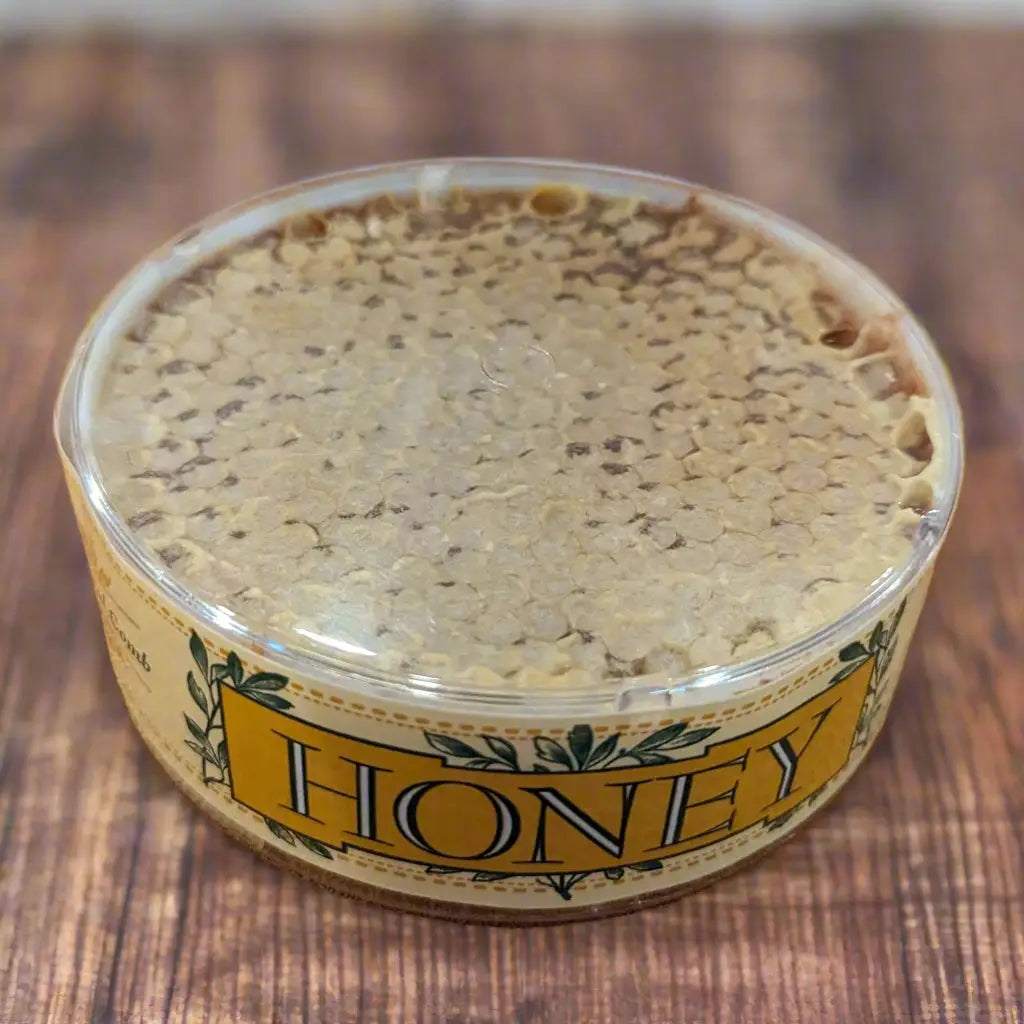 MOON'S GOLD COMB wildflower honey in a clear round tub, with pale golden honeycomb and a yellow “Honey” label.