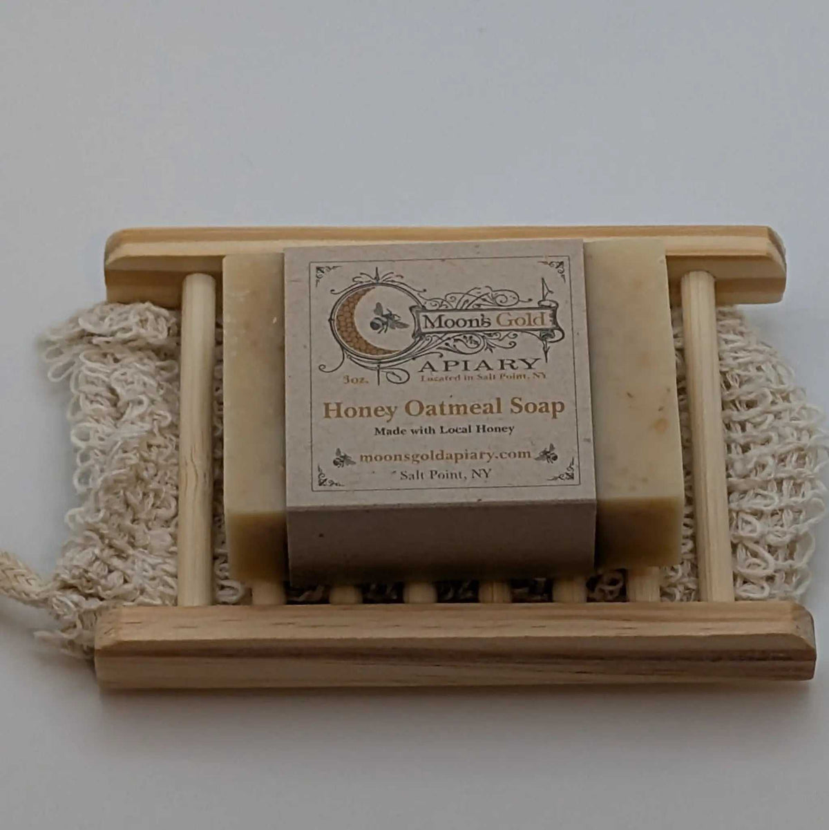 MOON'S GOLD SOAP BUNDLE with a beige honey oatmeal soap bar on a wooden slatted tray, paired with a cream knitted soap saver bag.